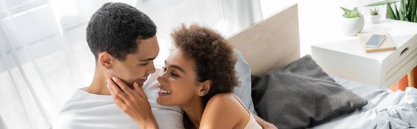 mujer afroamericana complacida tocando la cara del novio feliz en el dormitorio, pancarta - Foto, Imagen