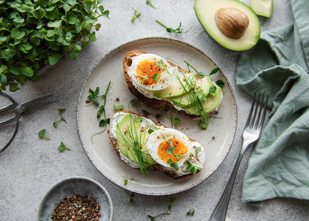 Bread toast, boiled eggs, avocado slice, microgreens on a plate, breakfast time - Фото, изображение
