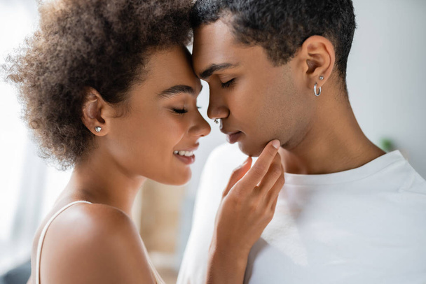 side view of smiling and tender african american woman touching chin of young boyfriend - Foto, afbeelding