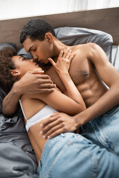 top view of muscular african american man hugging and kissing seductive girlfriend on bed  - Fotoğraf, Görsel