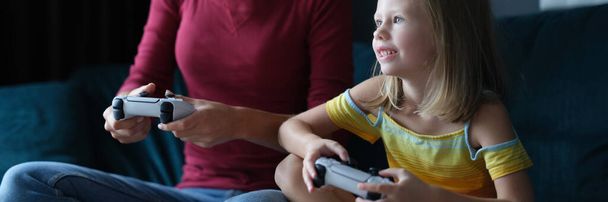 Mom and daughter hold game joysticks and play online games. Family games in game console concept - Fotó, kép