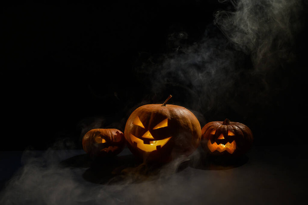 Pumpkins with carved grimaces and candles inside in the dark for halloween. Jack o latern in smoke - Foto, imagen