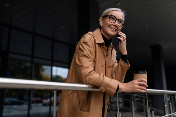 Business woman with a cup of coffee in her hands talking on a mobile phone. - Photo, Image