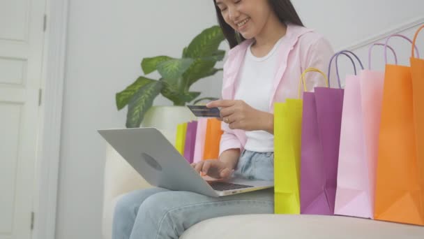 Молода азіатка, що сидить на дивані, використовуючи покупки ноутбуків онлайн з кредитною карткою, купуючи в Інтернеті, щаслива дівчина платить за транзакцію фінансову, покупку та оплату, бізнес-концепція
. - Кадри, відео