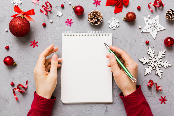 Noel 'i yazmak için bir kadın not defterine Xmas dekorasyonlu renkli arkaplan çiziyor. - Fotoğraf, Görsel