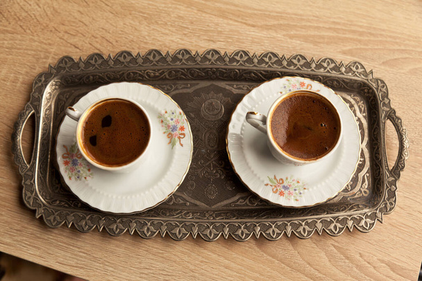 Традиционный пенный турецкий кофе в узорчатой белой чашке в металлическом подносе на дубовом кофейном столике - Фото, изображение