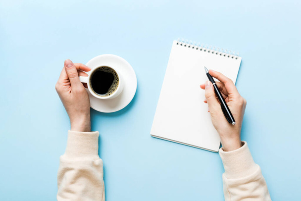 Kobieta ręka z ołówkiem na notatniku i trzymać filiżankę kawy. Kobieta pracująca na stole biurowym z kawą. - Zdjęcie, obraz