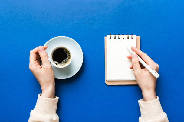 Mano de mujer con lápiz escrito en el cuaderno y sostenga la taza de café. Mujer trabajando en mesa de oficina con café. - Foto, Imagen