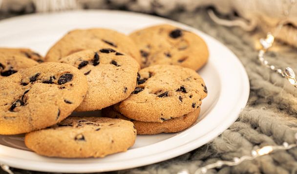 Primo piano di biscotti di gocce di cioccolato su un piatto su uno sfondo sfocato con una ghirlanda. - Foto, immagini