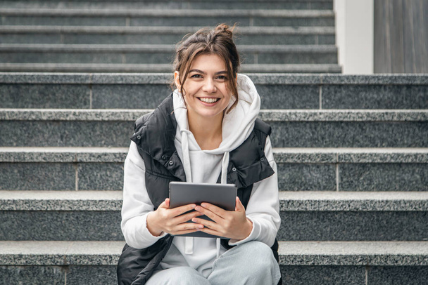 Młoda studentka siedzi na schodach z cyfrowym tabletem w rękach, koncepcją technologii i edukacji, przestrzenią do kopiowania. - Zdjęcie, obraz