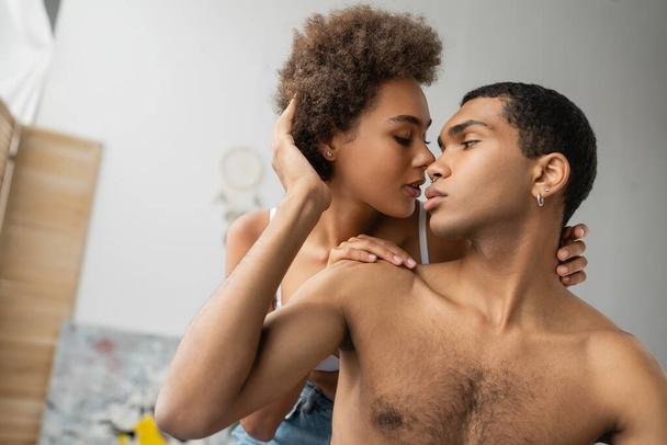 curly brunette woman hugging shirtless pierced african american boyfriend at home - Foto, afbeelding
