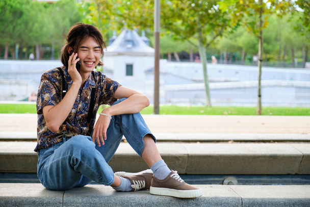 Joven taiwanés sonriendo y hablando en el teléfono inteligente en la calle. - Foto, imagen