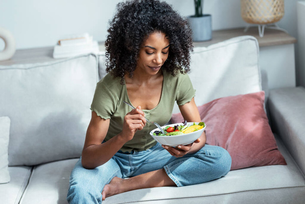 美しいです女性のショット食べる健康的なサラダながら座っていますソファに家. - 写真・画像