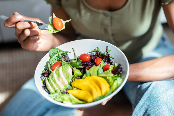 Shot of beautiful woman eating healthy salad while sitting on couch at home. - Fotó, kép