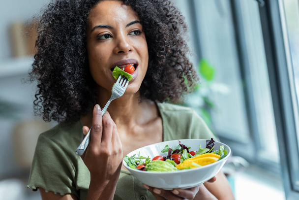 Shot of beautiful woman eating healthy salad while sitting on couch at home. - Zdjęcie, obraz