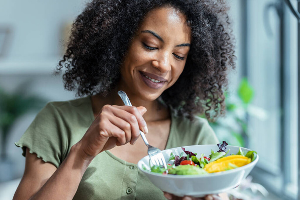 Shot of beautiful woman eating healthy salad while sitting on couch at home. - Photo, image