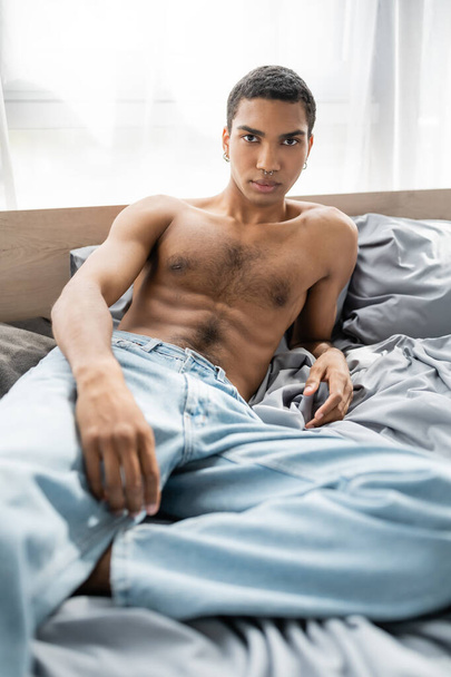 sexy and muscular african american man in jeans looking at camera on grey bedding, banner - Foto, immagini