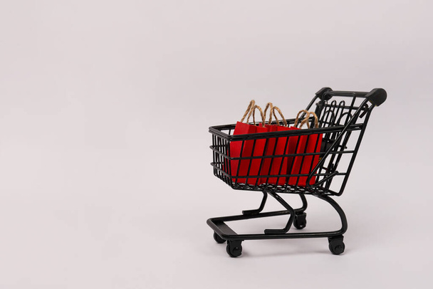 Black shopping cart with red paper bags on gray background, copy space. black friday concept - Fotoğraf, Görsel