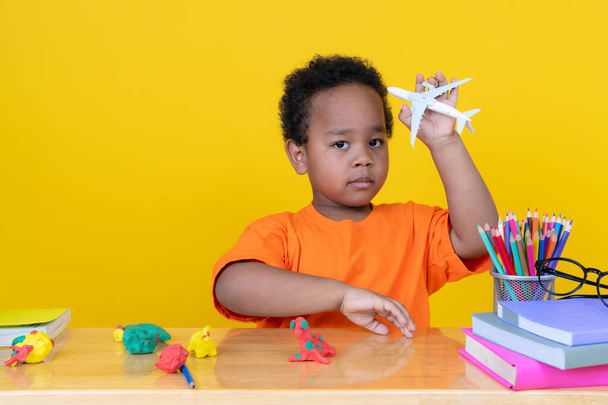 Mały chłopiec Wyobraź sobie bycie pilotem bawiącym się samolotem zabawki na żółtym tle. - Zdjęcie, obraz