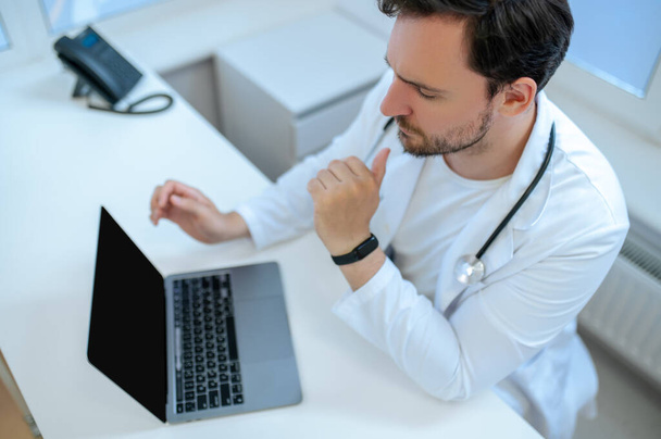 Doctors office. Bearded young doctor sitting at the laptop in his office - 写真・画像