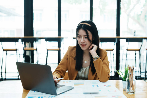 Портрет вдумчивой азиатской предпринимательницы, смотрящей на финансовые отчеты и строящей маркетинговые планы с помощью компьютера на столе. - Фото, изображение