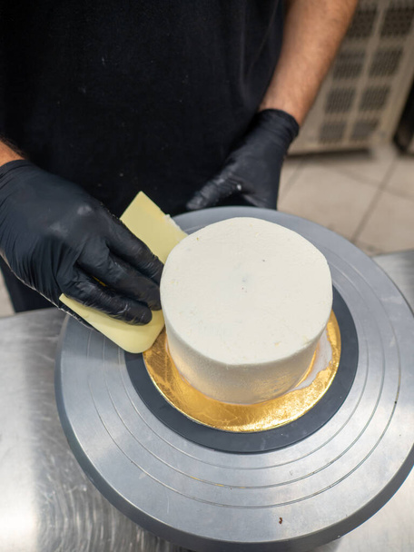 Decorador usando espátula y rascador para suavizar la crema de mantequilla en un pastel helado - Foto, Imagen