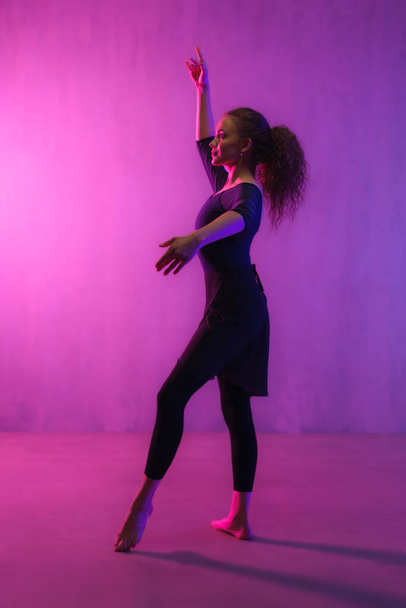 A modern dance girl dancer dancing in neon light doing gymnastic exercises in studio, copy space. - Foto, immagini