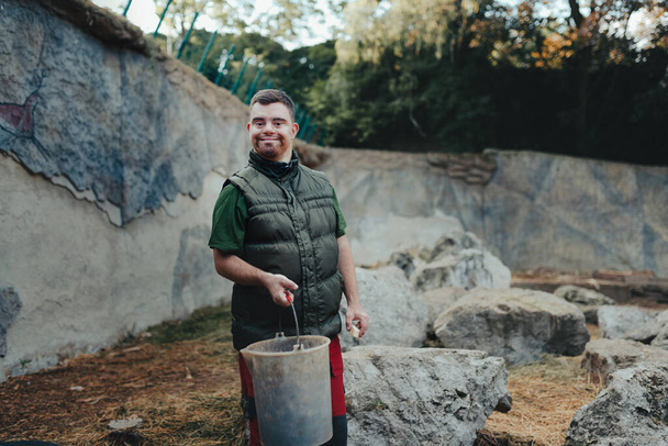 Caretaker with down syndrome in the zoo giving food in animal enclosure. Concept of integration people with disabilities into society. - Fotografie, Obrázek