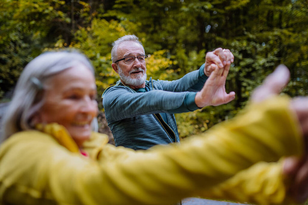 Senior couple doing stretching during hiking in autumn forest. - Photo, Image