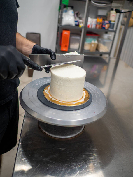 Decorador usando espátula y rascador para suavizar la crema de mantequilla en un pastel helado - Foto, imagen