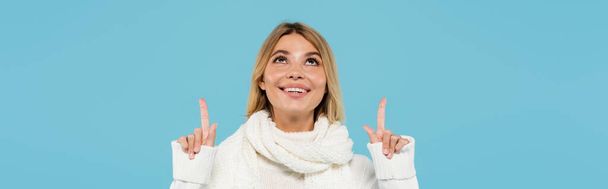 fröhliche blonde Frau in weißem Pullover und Schal, die mit den Fingern nach oben zeigt, auf blauem Banner - Foto, Bild