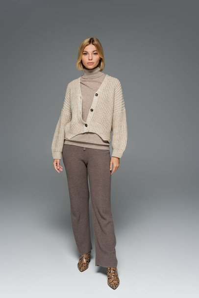 full length of young woman in turtleneck and cardigan standing on grey - Φωτογραφία, εικόνα