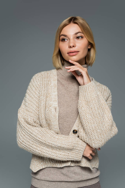 young blonde woman in turtleneck and cardigan looking away isolated on grey - Photo, Image