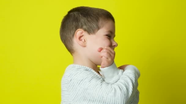 Een gelukkige 5-jarige jongen lacht en kijkt weg, kruist zijn armen op zijn borst op een gele achtergrond. - Video