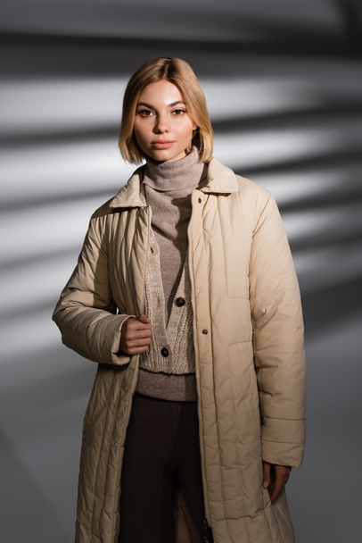 Pretty woman in beige winter outfit looking at camera on abstract grey background  - Photo, Image