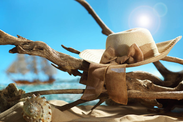 Sombrero de verano de paja vintage colgando de la parte superior de madera a la deriva en una playa de arena - Foto, imagen