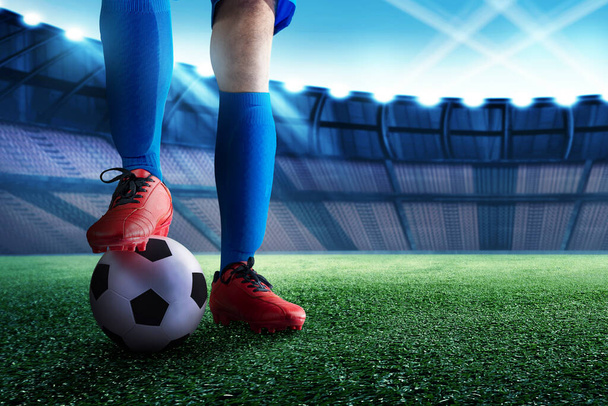 Футболист в синей майке стоит с мячом на футбольном поле - Фото, изображение