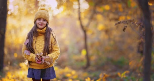 Szczęśliwa dziewczyna bawi się kolorowymi jesiennymi liśćmi w lesie w słoneczny jesienny dzień. Beztroska kobieta biegać w parku ścieżka, jesień krajobraz 4k wideo - Materiał filmowy, wideo