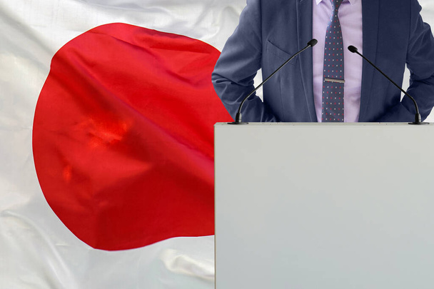 Tribune s mikrofonem a muž v obleku na pozadí japonské vlajky. Podnikatel a tribun na pozadí japonské vlajky. Politik na pódiu s mikrofony na pozadí japonské vlajky. Obchodní konference - Fotografie, Obrázek