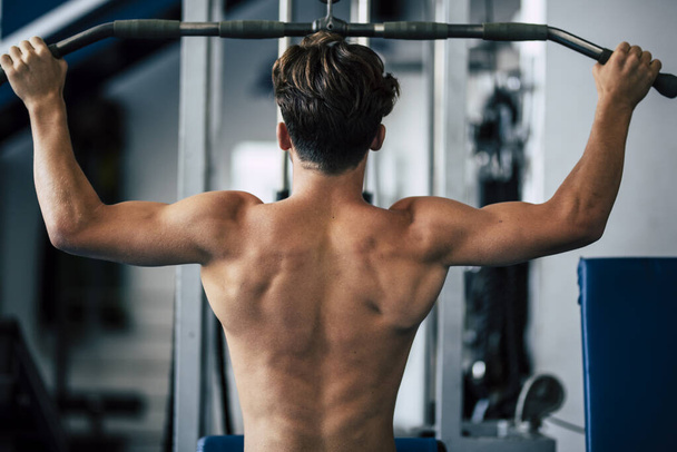 teenager without t-shirt at the gym doing exercise for his back - man training hard with weights to be a fitness and healthy man lifestyle   - Photo, image