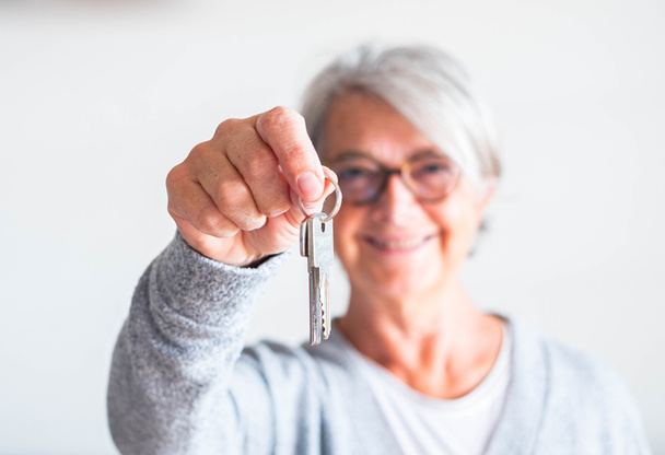 una donna anziana e matura in possesso di una chiave di una casa o di una macchina - vende la sua proprietà a qualcuno pronto ad affittare o acquistare   - Foto, immagini