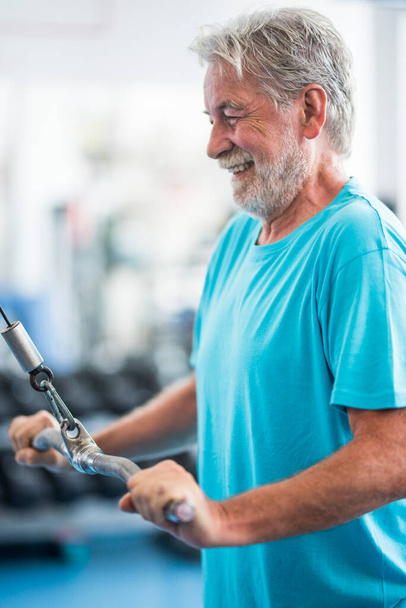 jeden dojrzały mężczyzna podnoszący ciężar z maszyną na siłowni - aktywny trening seniorów ciężko sam - zdrowy i sprawny mężczyzna  - Zdjęcie, obraz