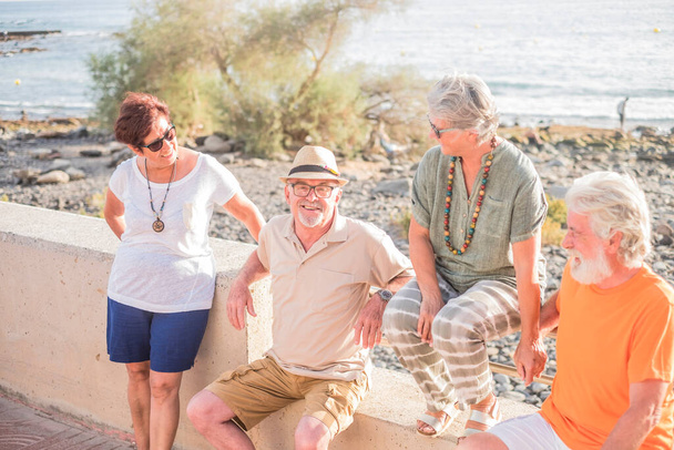 grupo de personas mayores y personas maduras sentadas en la playa en un banco - feliz amistad con dos parejas de jubilados casados hablando y divirtiéndose   - Foto, imagen