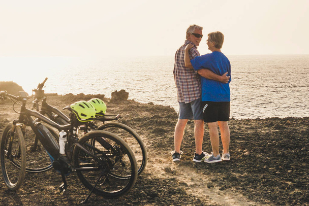 bella coppia di anziani abbracciati in spiaggia o in un parco con le loro biciclette - formazione di persone mature e attive e lavoro duro per essere fitness  - Foto, immagini