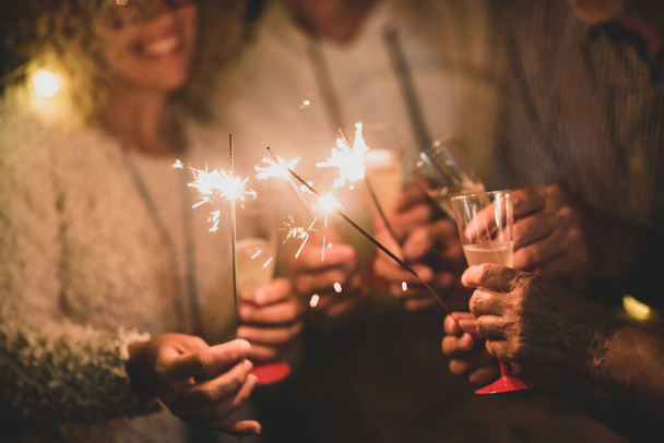 grupo de cuatro personas divirtiéndose y disfrutando sosteniendo copas de champán y bengalas celebrando el feliz año nuevo juntos   - Foto, Imagen