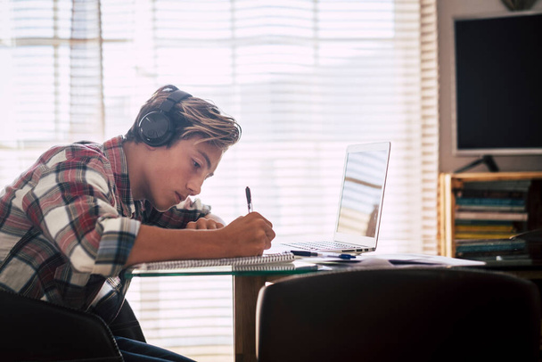 Közelkép tinédzser fülhallgató bámul laptop csinál a házi feladatot csendben - beltéri fókusz srác  - Fotó, kép