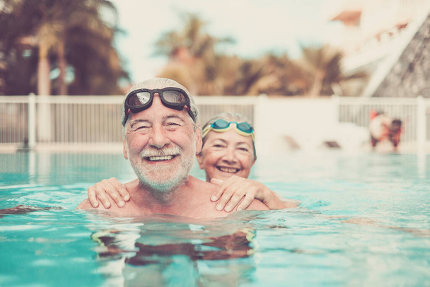 two seniors at the pool hugged together and playing - happy mature people and couple of pensioners looking at the camera smiling  - Photo, Image