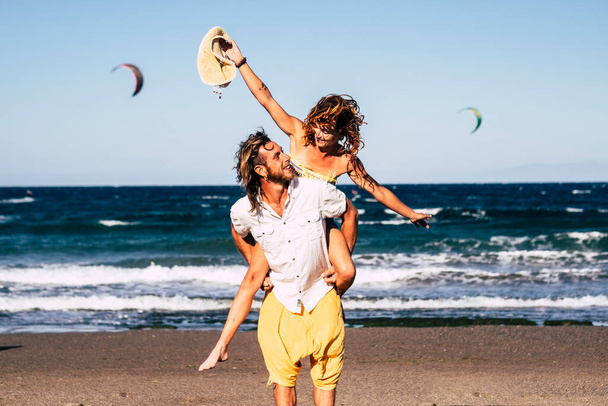 piękna para dorosłych bawiących się razem na plaży na piasku - mężczyzna spacerujący z żoną lub jego dziewczyna na on - on trzyma ją - kobieta z otwartymi ramionami być szczęśliwym  - Zdjęcie, obraz