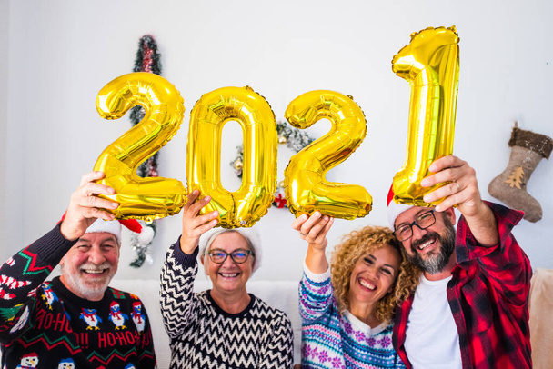 cuatro personas se divierten y sonríen juntas en casa sosteniendo los números de los cuatro globos del 2021 - la familia riendo y celebrando la Navidad y el año nuevo  - Foto, imagen