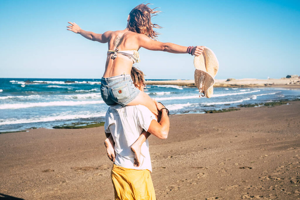 couple of beautiful adults get engaged and married together at the beach - woman on the shoulders of the man looking at him and smiling  - Photo, Image